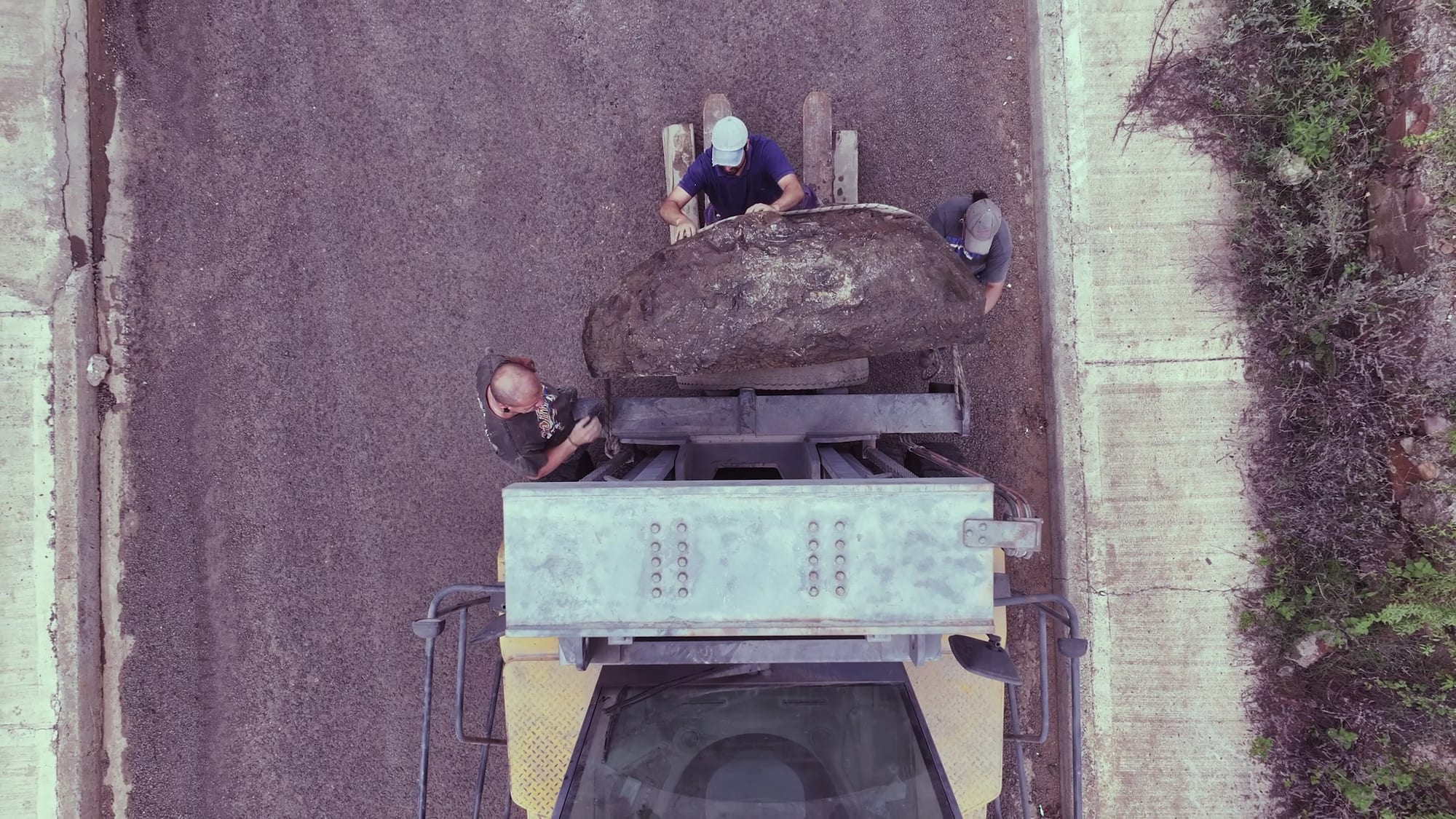Pala cargadora transportando un bloque de roca por el camino de la cantera, con dos personas sobre la carga, visto desde arriba