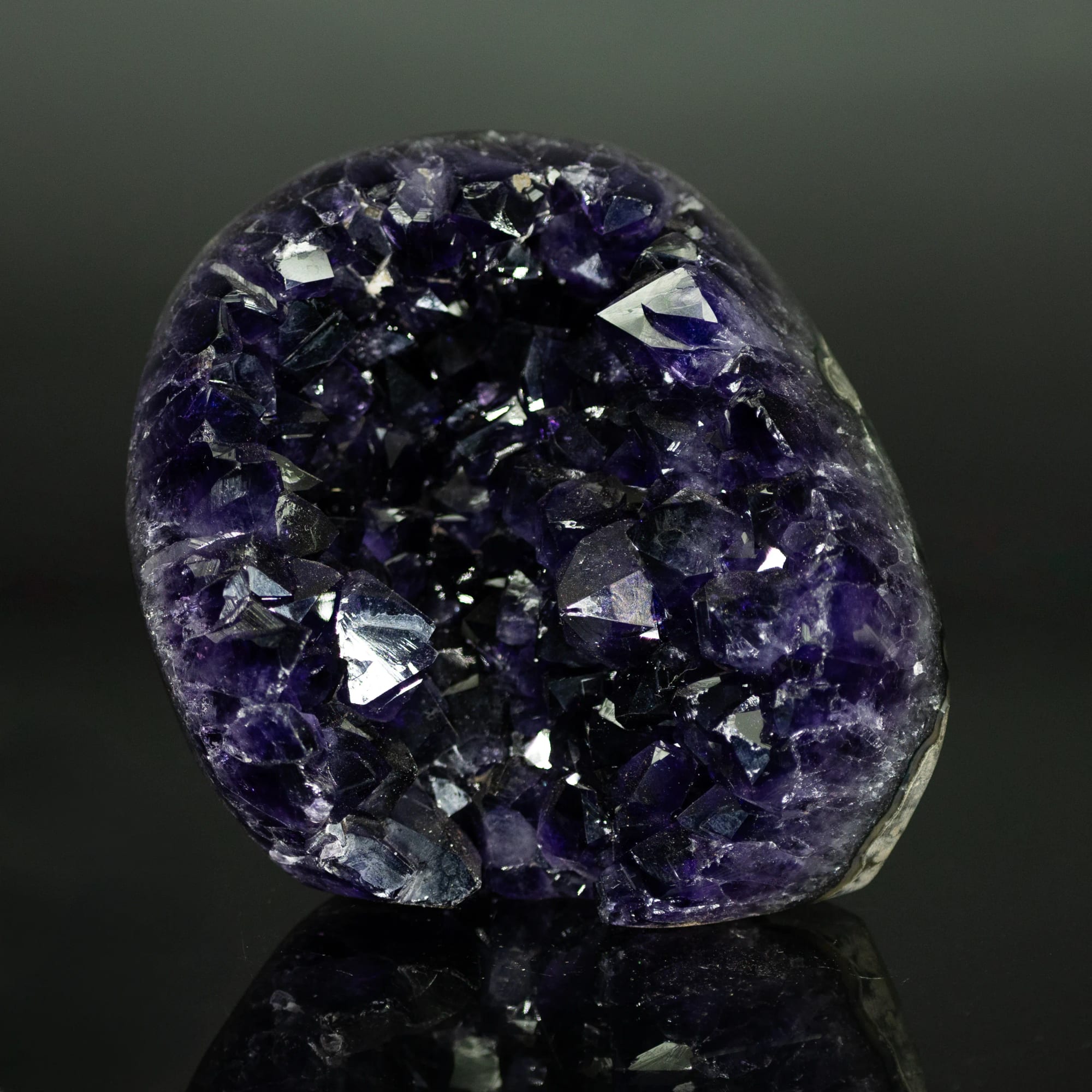 Geoda de amatista violeta profunda, forma redondeada, sobre fondo negro con reflejo